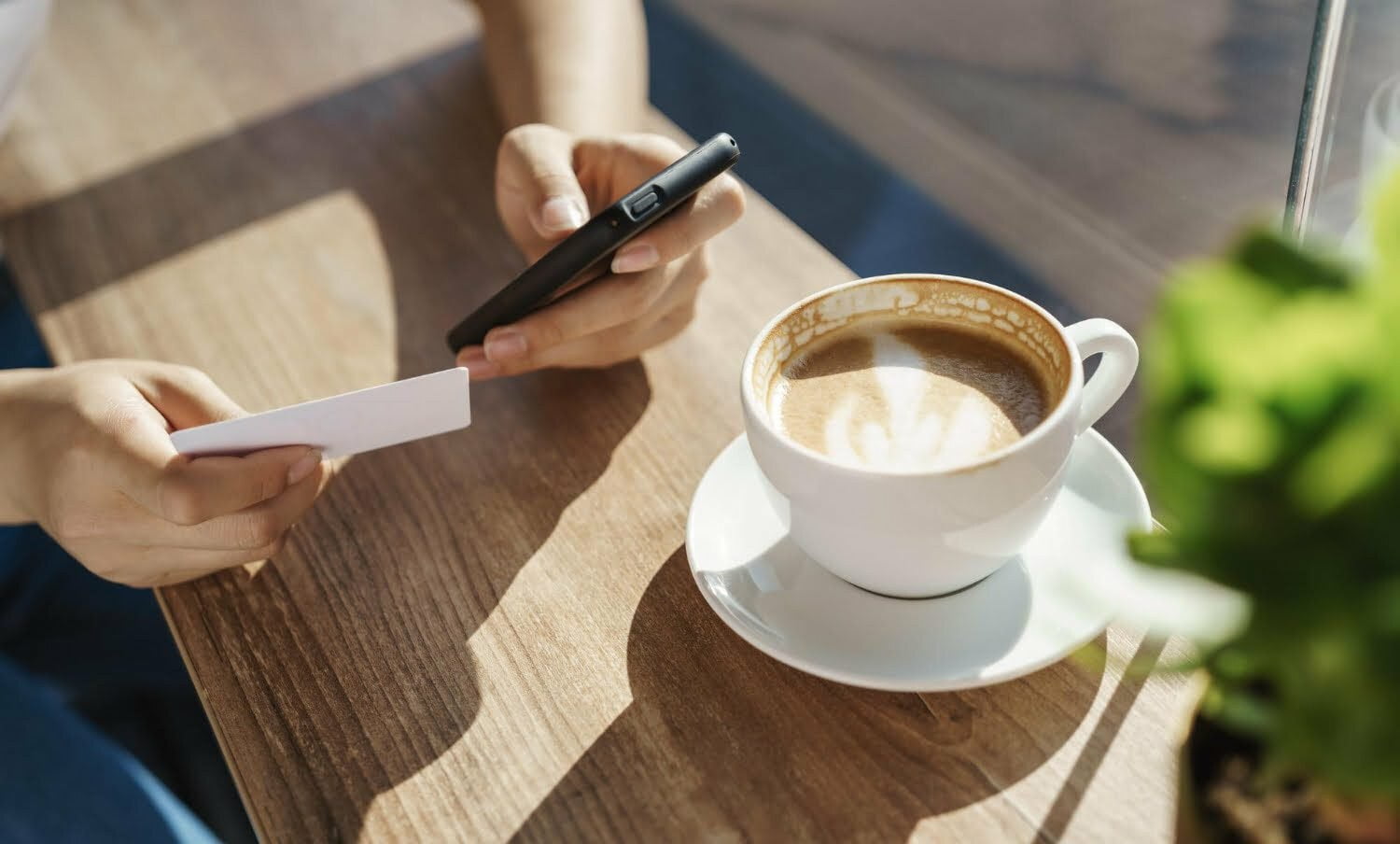 persona con una taza de café en una mesa y el celular en la mano