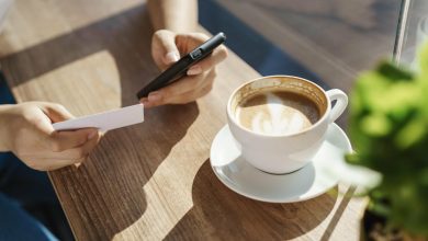 persona con una taza de café en una mesa y el celular en la mano