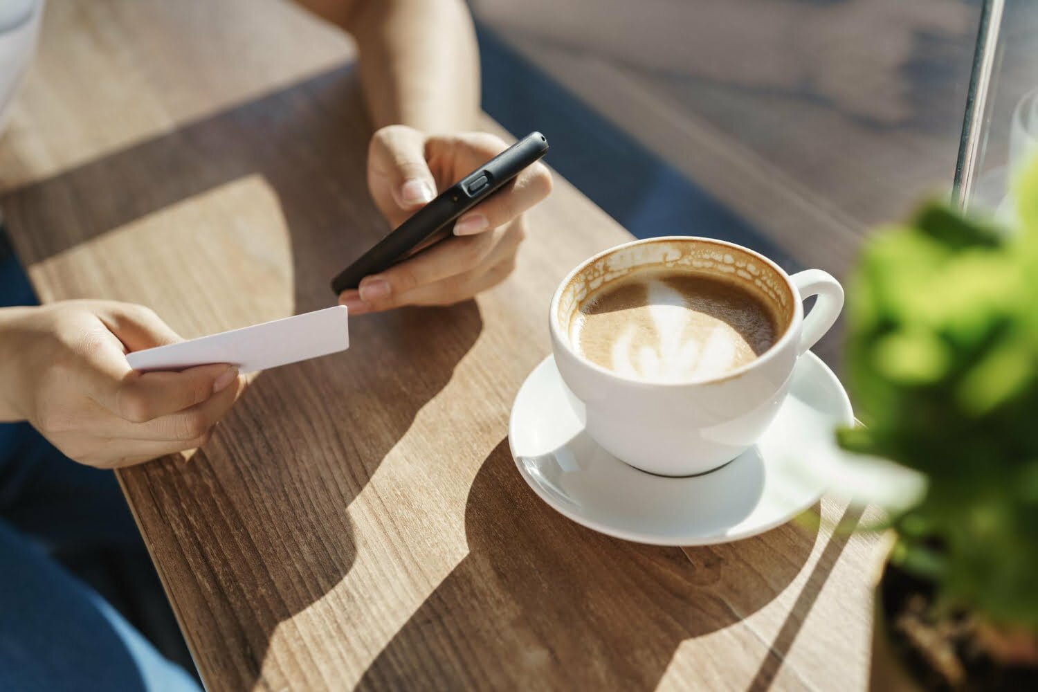 persona con una taza de café en una mesa y el celular en la mano