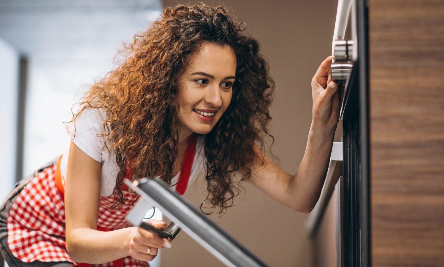 mujer de cabello rizado mira hacia el interior de su horno con la puerta abierta