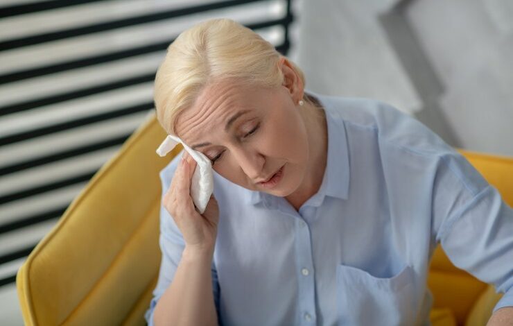 Caliente, sintiéndose mal. mujer rubia con los ojos cerrados limpiándose la cara con una frente menopausia