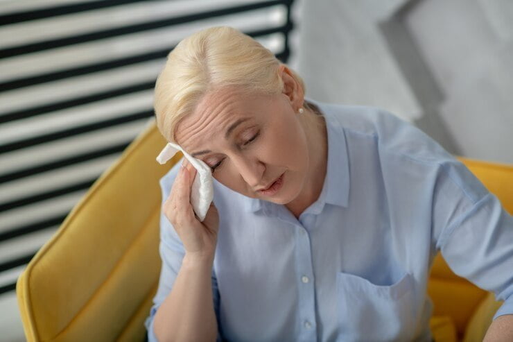 Caliente, sintiéndose mal. mujer rubia con los ojos cerrados limpiándose la cara con una frente menopausia