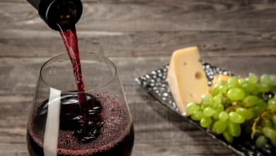 Una botella y una copa de vino tinto con frutas sobre mesa de madera