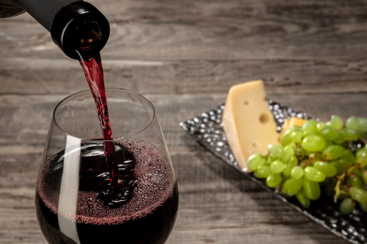 Una botella y una copa de vino tinto con frutas sobre mesa de madera