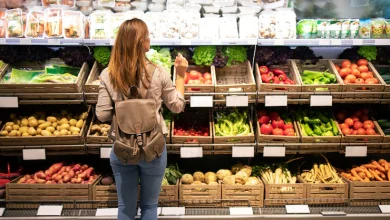 Buena mujer de pie delante de los estantes de verduras eligiendo qué comprar fruta