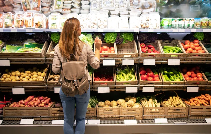 Buena mujer de pie delante de los estantes de verduras eligiendo qué comprar fruta