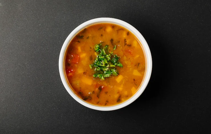 sopa de lentejas con ingredientes mixtos y hierbas en un tazón blanco.