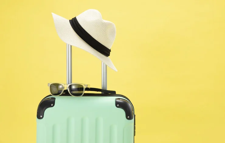 Vista superior de una maleta, gafas de sol, cámara y sombrero sobre un fondo amarillo