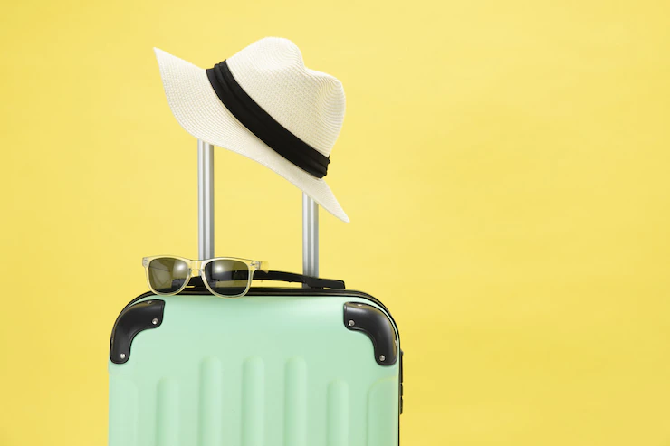 Vista superior de una maleta, gafas de sol, cámara y sombrero sobre un fondo amarillo
