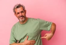 hombre caucásico de mediana edad aislado sobre fondo rosa con dolor de hígado, dolor de hernia