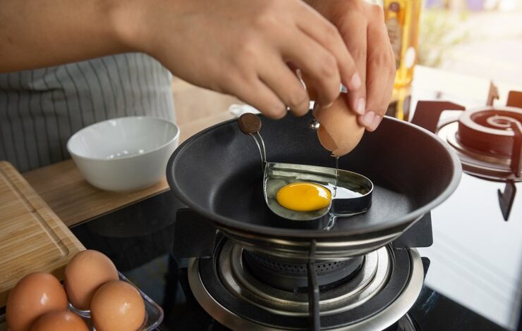 persona rompiendo un huevos en molde de corazón en una sartén