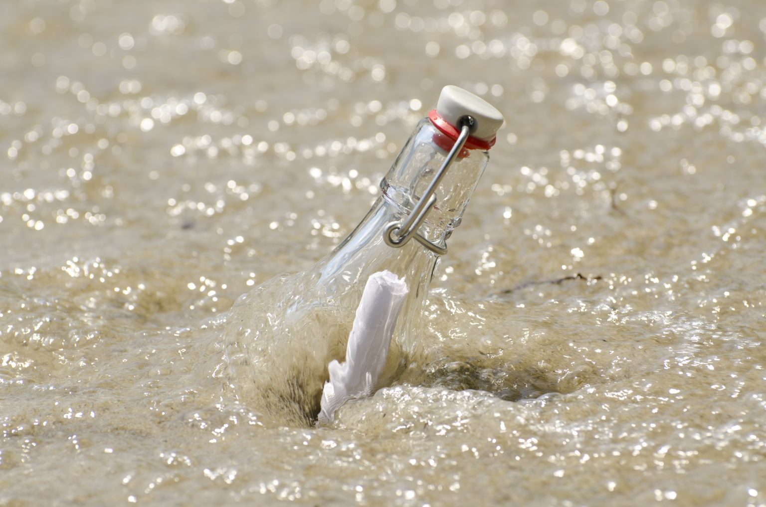 primer plano de un mensaje en una botella en la arena con agua en un día soleado mar