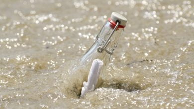 primer plano de un mensaje en una botella en la arena con agua en un día soleado mar