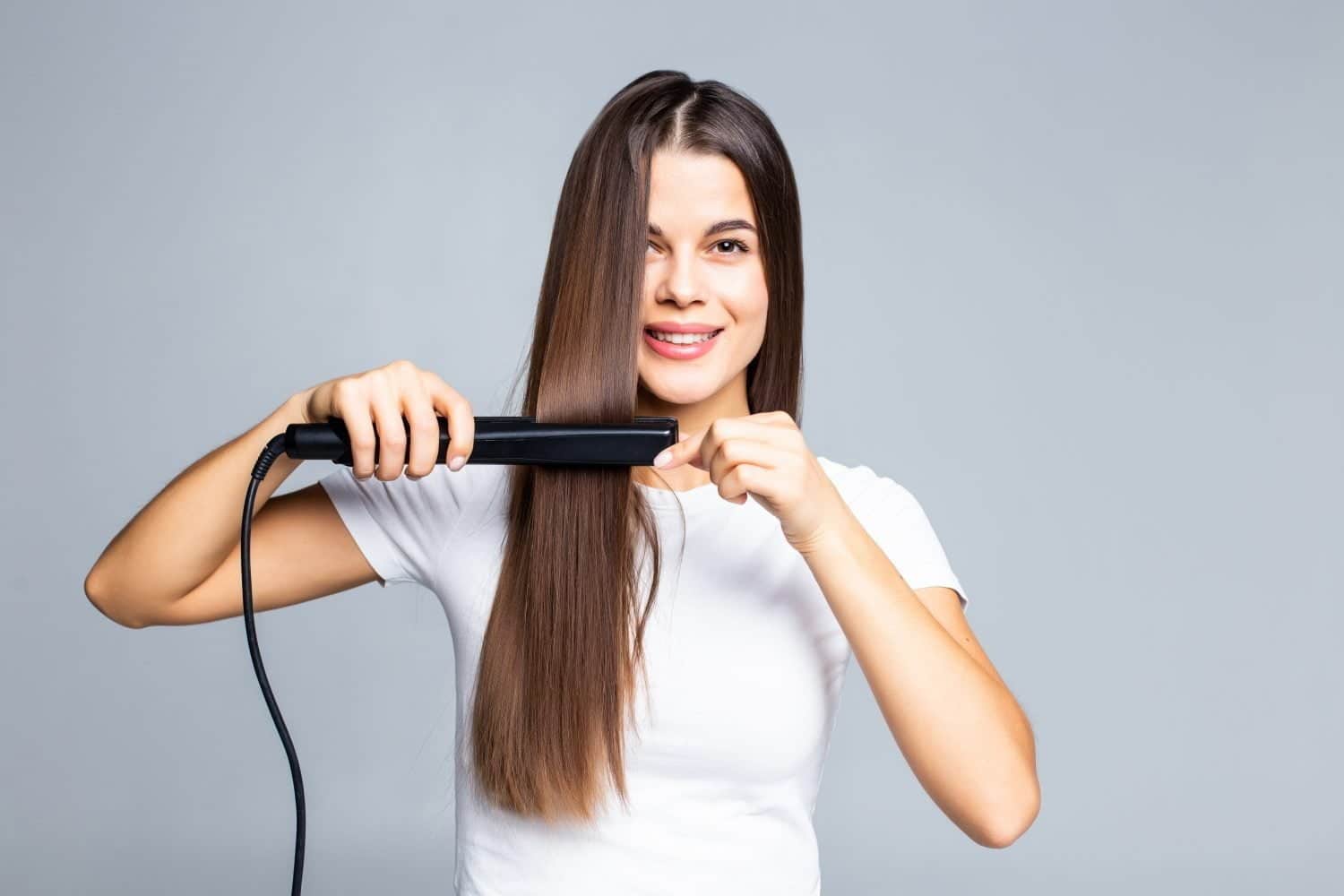 mujer joven sonriente que se endereza el pelo con blanco