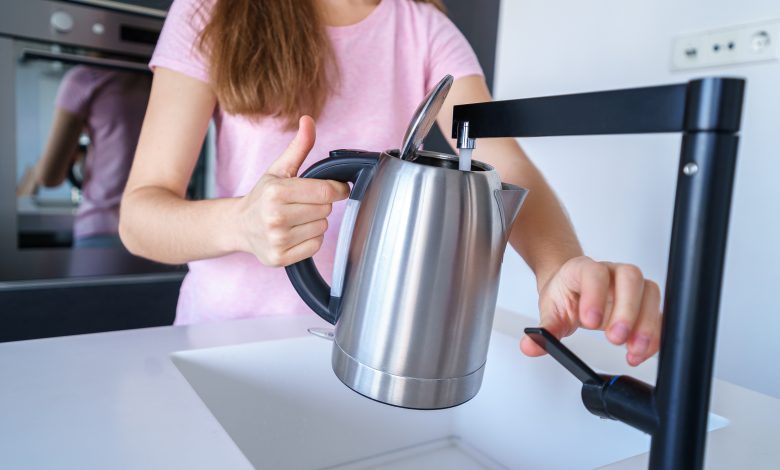 la mujer vierte agua limpia, fresca, filtrada y purificada de un grifo en una tetera eléctrica para