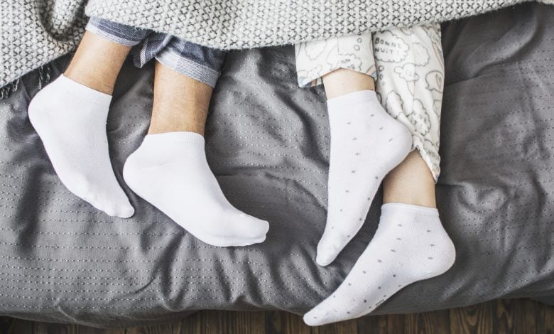 piernas masculinas y femeninas en calcetines debajo de una manta en una cama
